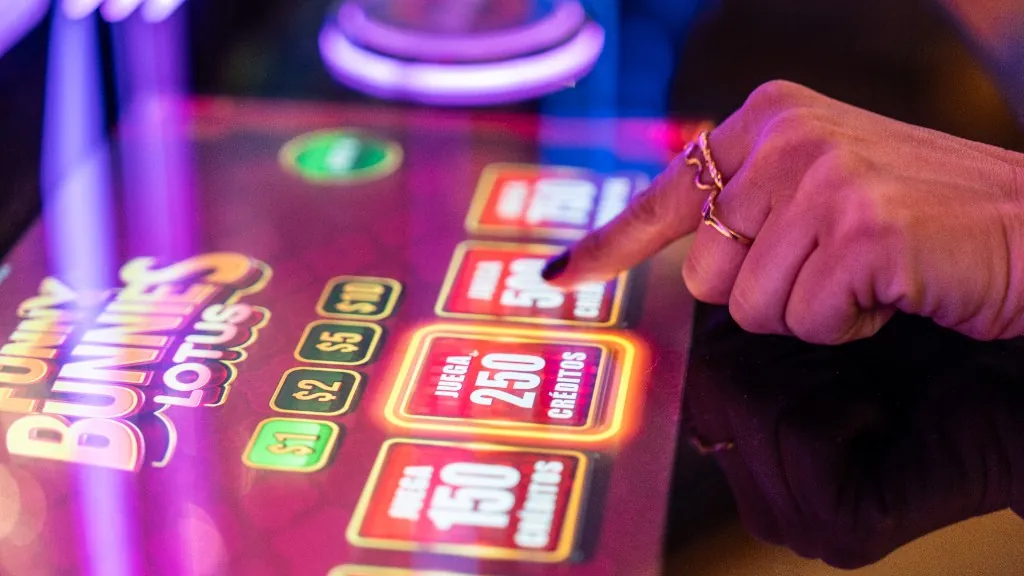 Mano pulsando el botón de jugar en una máquina de slots de Casino Arena Maipú